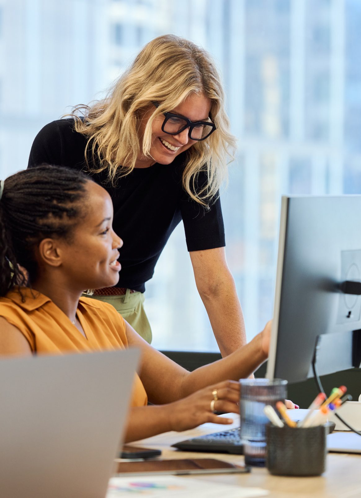 Business professionals collaborating at a computer in a modern office, showing teamwork, mentorship, and positive workplace culture.