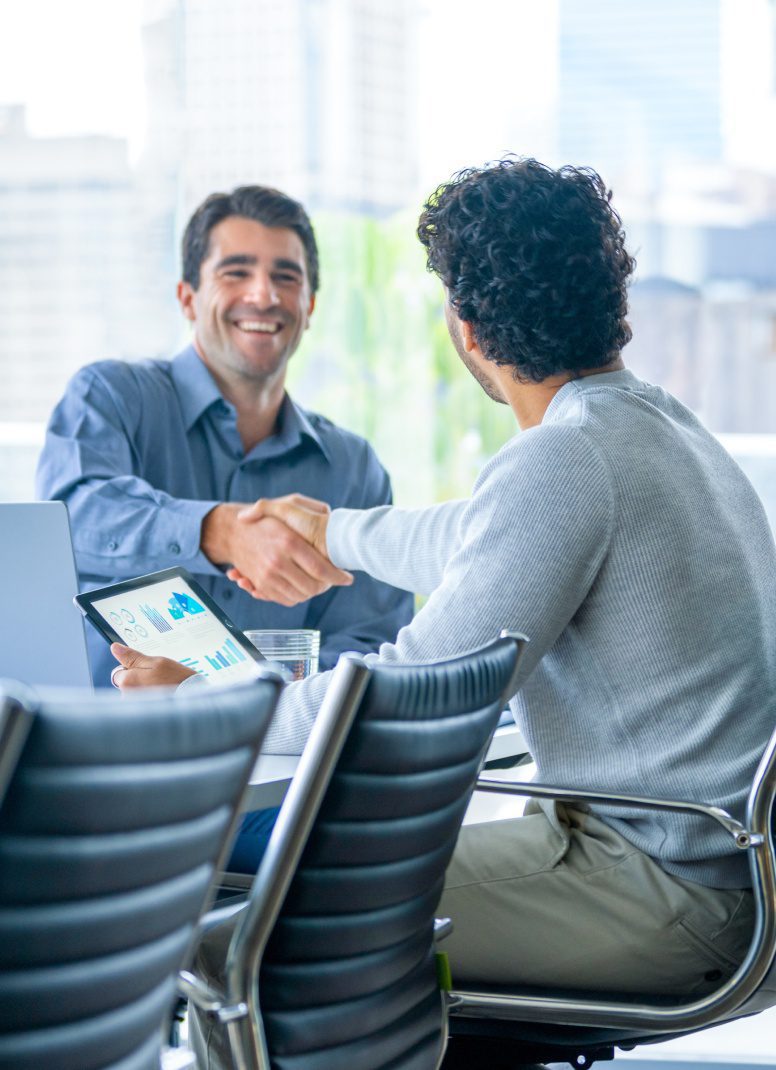 Two men shake hands across a conference table during a meeting.